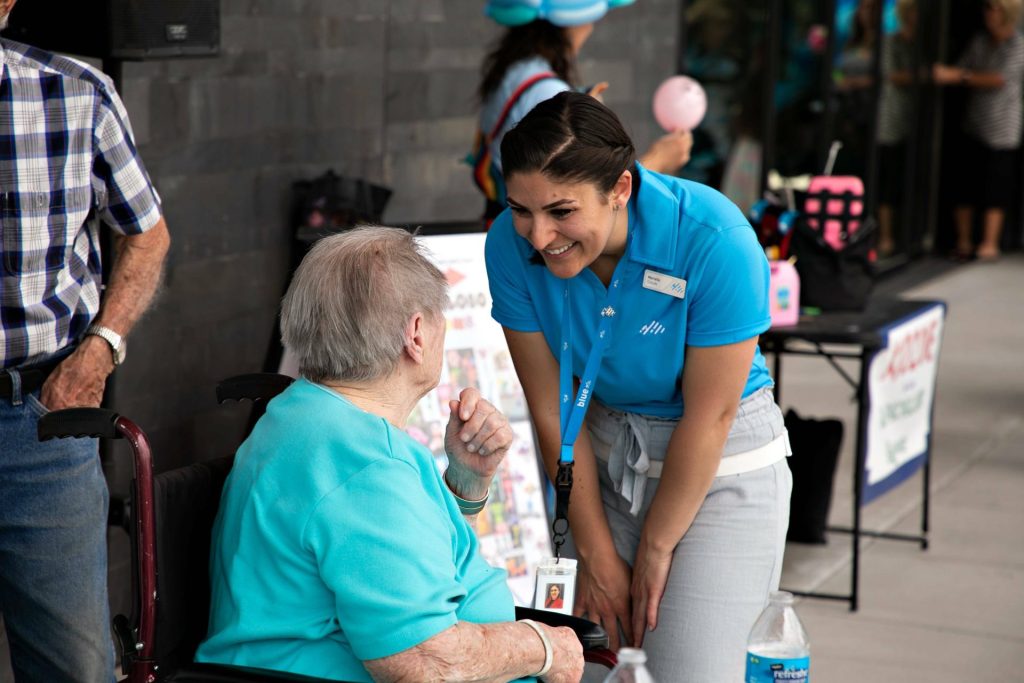 Blue employee leaning down to talk with an older member.