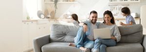 A young family sitting on the couch looking at a laptop