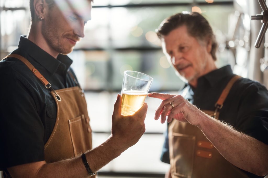 Two brewers viewing a glass of beer. Blue Partnership