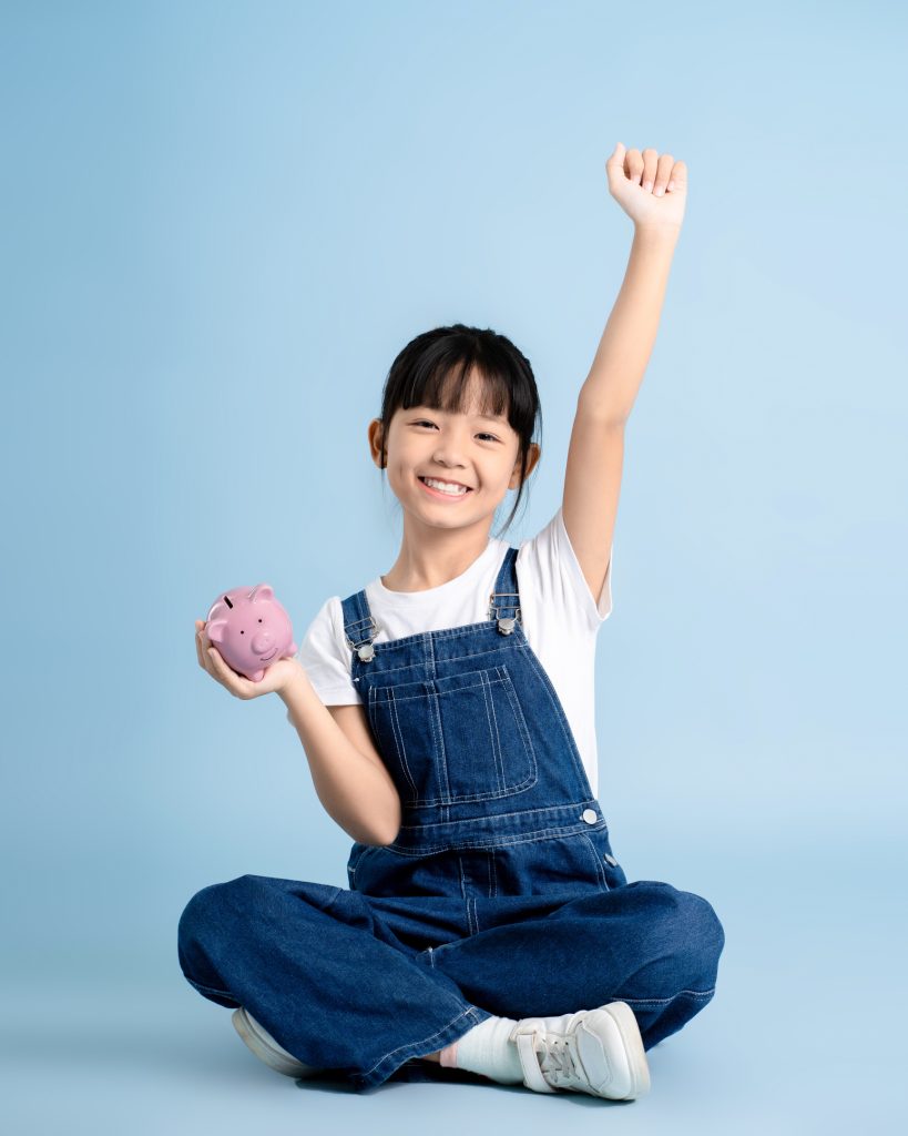 asian girl sitting and holding piggy bank on blue background